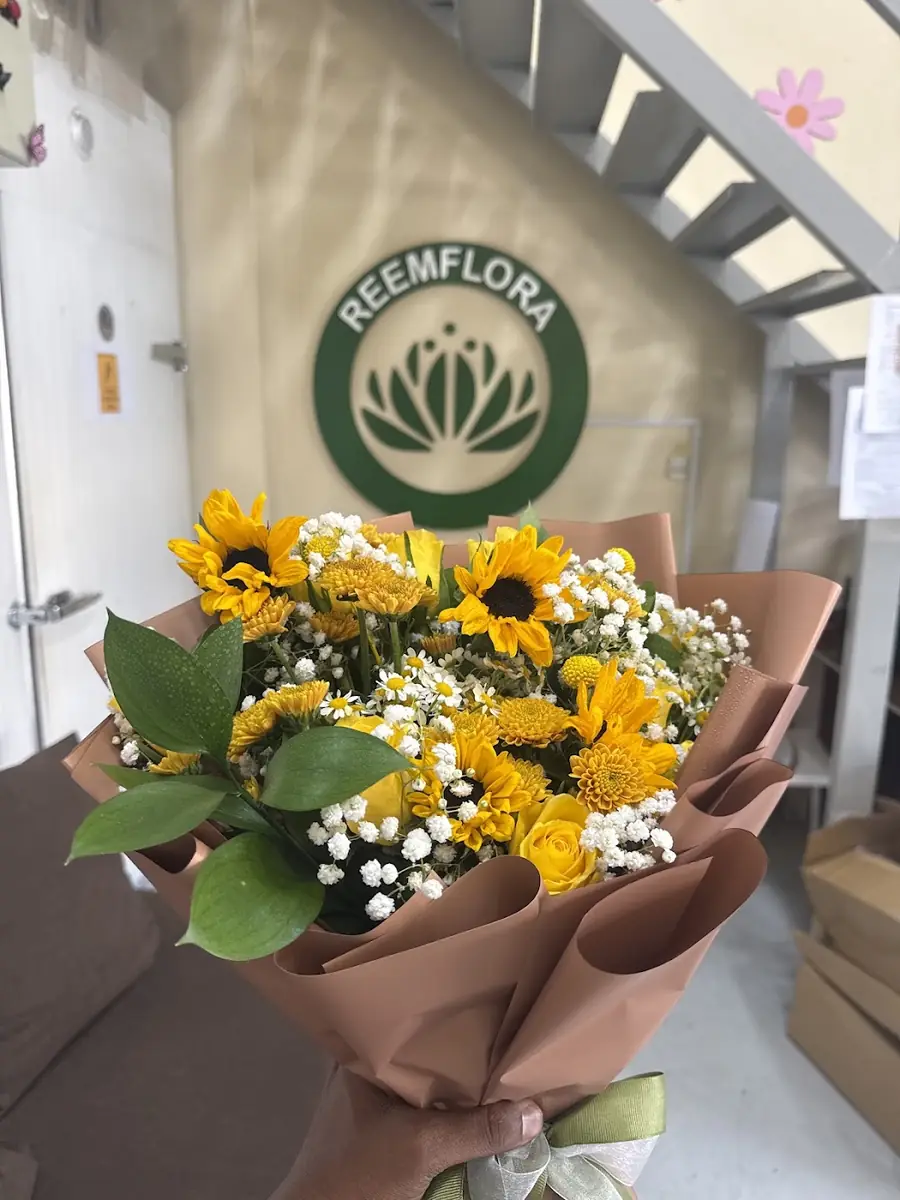 A sunflower and chrysanthemum bouquet held in front of the Reemflora sign at the warehouse